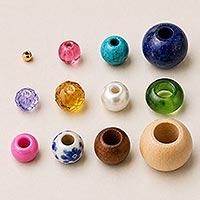 Assorted beads in various materials, colors, and styles arranged by progressively larger hole sizes, from a tiny seed bead to a large wood macrame bead.