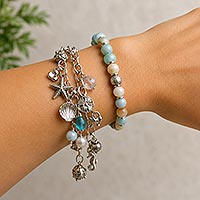 Close-up of a lower arm wearing two bracelets, including a snug-fitting beaded bracelet and a loose dangling charm bracelet demonstrating different bracelet styles and fits.